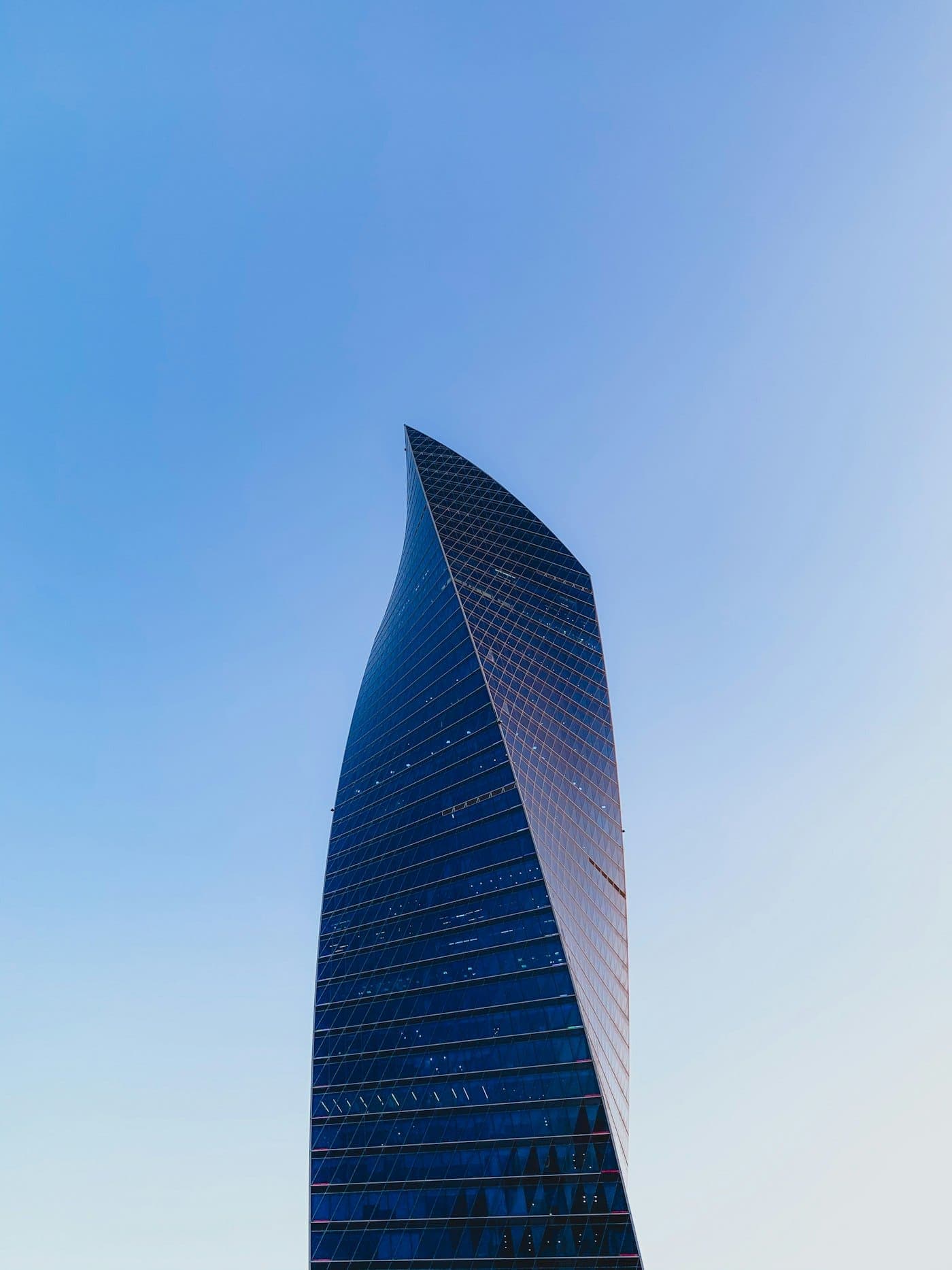 Tall black and gray glass high-rise building under a bright daytime sky