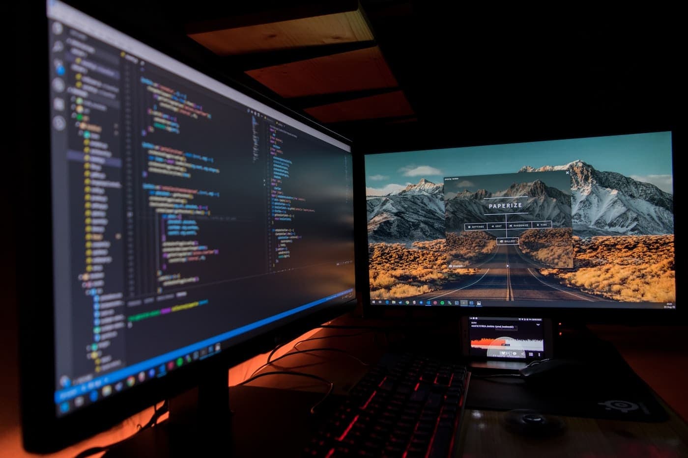 Two black flat-screen developer monitors glowing in a dark room